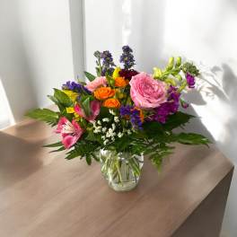 Mixed bouquet in a clear glass vase with pink, orange, purple, and yellow flowers