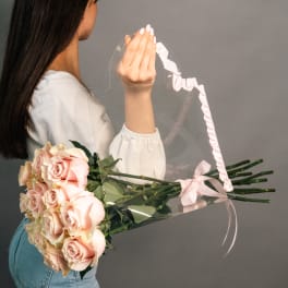 Woman holding a bouquet of pale pink roses wrapped in clear plastic
