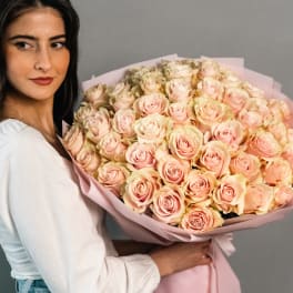 Woman holding a large bouquet of pale pink roses wrapped in pink paper
