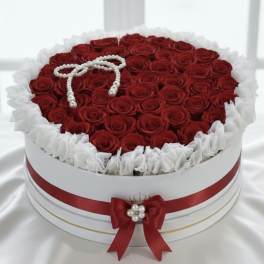 Round box filled with red roses and white ruffled trim, topped with a pearl bow