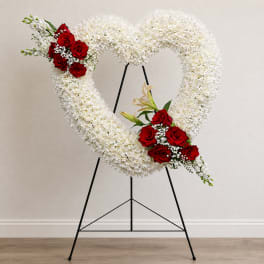 Heart-shaped white floral wreath with red rose clusters on a black stand