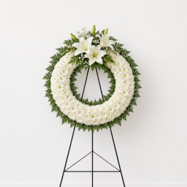 White floral wreath on a black easel with lilies and daisies