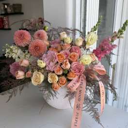 Mixed pink and peach flowers arranged in a white vase with ribbon.
