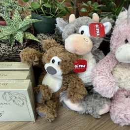 Three plush unicorn toys sit beside potted plants.