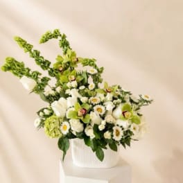 White and green floral arrangement in a ribbed white container