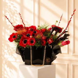 Red floral arrangement in a black gift bag with gold chain handles