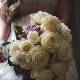 Bride holding a bouquet of cream roses and pale purple flowers