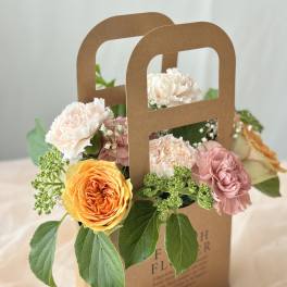 Mixed flowers arranged in a brown paper gift bag with handle cutouts