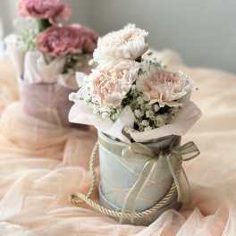 Pink carnations in a ribbon-tied gift box with baby's breath