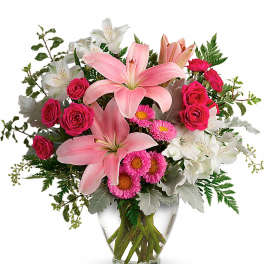 Pink lilies, hot pink roses, and white alstroemeria arranged in a clear glass vase