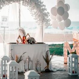 Beachside wedding table with white floral arch, balloons, and lanterns