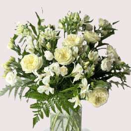 White flowers arranged in a clear glass vase with fern foliage