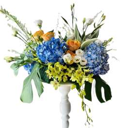 Blue hydrangea and orange rose arrangement in a white pedestal vase