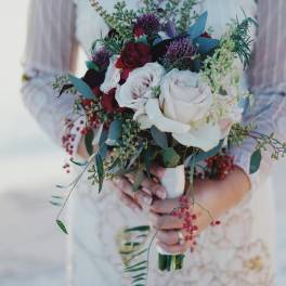Bride holding a bouquet of white and red roses with greenery