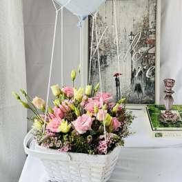 Pink and cream flowers in a white basket with a pale blue balloon