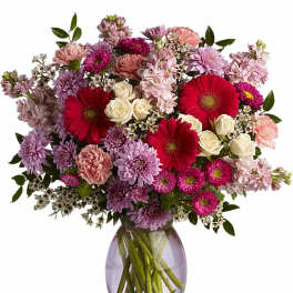 Mixed bouquet of pink and purple blooms with cream roses in a clear glass vase