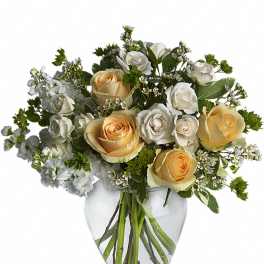 Peach and white rose bouquet with white filler flowers arranged in a clear glass vase