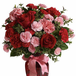 Red and pink carnations and roses in a red glass vase with a pink ribbon