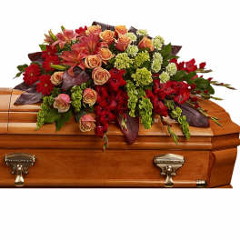 Long casket spray of red and peach flowers with green accents on a wooden casket