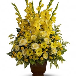 Tall yellow and white arrangement with gladiolus, roses, and daisies in a dark pedestal vase