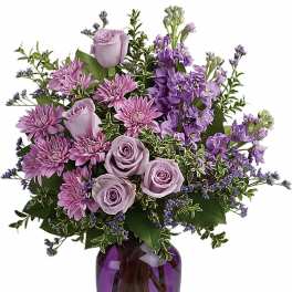Arrangement of lavender roses and purple flowers in a purple glass vase