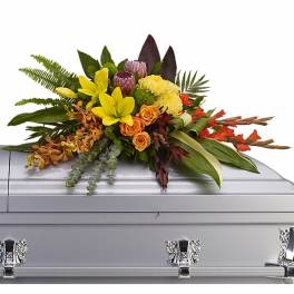 Tropical casket spray of yellow lilies, orange roses, orchids, and protea on a silver casket.