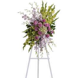 Standing spray with lavender roses, white orchids, and green flowers on a white easel