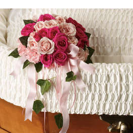 Pink rose casket bouquet with satin ribbons resting on a white lined casket