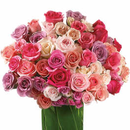Round arrangement of pink and pastel roses in a glass vase lined with green leaves