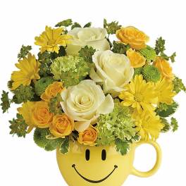 Yellow and white roses, daisies, and green accents arranged in a yellow smiley-face mug
