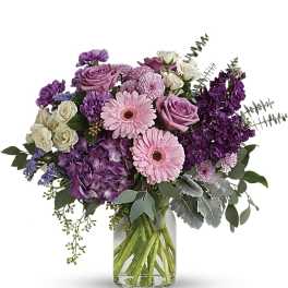 Mixed bouquet of pink gerbera daisies, purple roses, and hydrangea in a clear glass vase