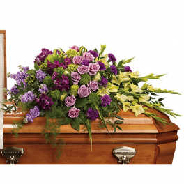 Lavender and purple casket spray with roses and yellow flowers arranged atop a wooden casket