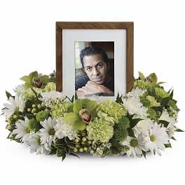 Low white and green flower wreath encircling a wooden photo frame with a portrait at the center