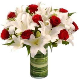 Red roses and white lilies arranged in a green glass vase