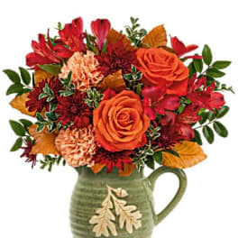 Orange and red bouquet in a green ceramic pitcher vase