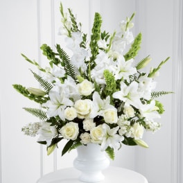 Tall white arrangement of lilies, roses and carnations in a white pedestal vase