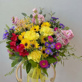 Colorful birthday bouquet with yellow, pink, purple, and red flowers in a glass vase
