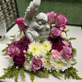 Pink roses and white chrysanthemums arranged around a small angel statue