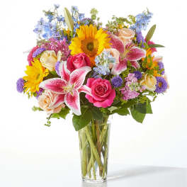 Mixed bouquet of sunflowers, roses, and lilies in a clear glass vase