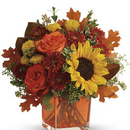 Autumn bouquet of roses, sunflowers, and mums in an orange glass vase