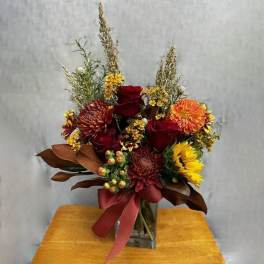 Autumn bouquet with red roses, orange blooms, and a burgundy ribbon in a glass vase