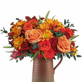 Orange and red flower arrangement in a brown pitcher vase