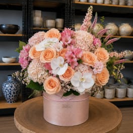 Peach and pink floral arrangement in a round pink box