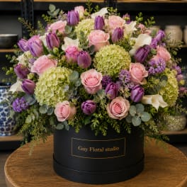 Pink roses and purple tulips arranged in a black hat box