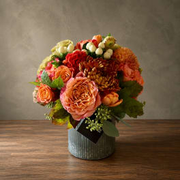 Mixed bouquet of orange, pink, and red flowers in a ribbed metal vase