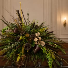 Large funeral spray with greenery, lotus pods, and beige ribbon on a casket