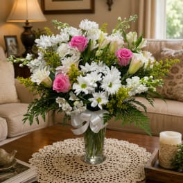 Pink roses and white daisies in a clear glass vase with a white ribbon