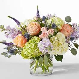Mixed bouquet of peach roses, hydrangeas, and purple flowers in a glass vase