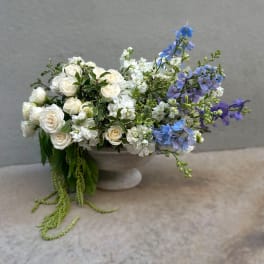 White roses and blue delphinium in a gray pedestal bowl