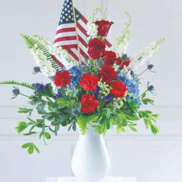 Red roses and blue-white flowers in a white vase with an American flag
